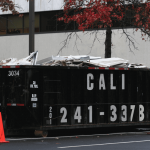 a black dumpster in a parking lot filled with various garbage and waste