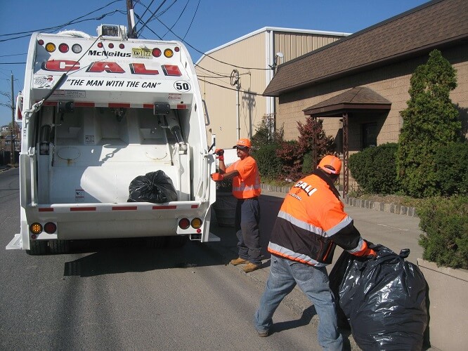 two male workers picking up trash and putting into the cali carting dumpster