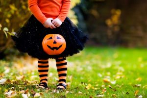 child in orange shirt, black skirt, and orange and black stripe stockings holding a jack-o-lantern for trick or treating